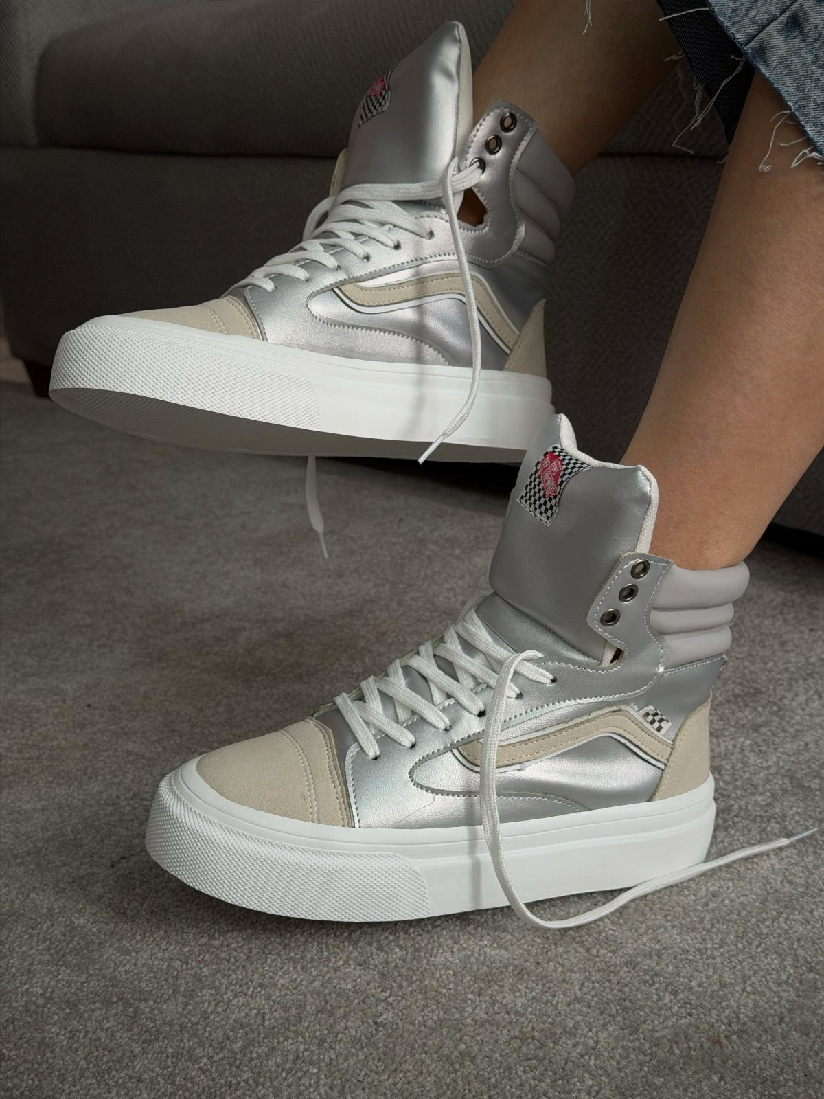 Silver metallic high-top sneakers with thick white platform soles on a grey carpet.