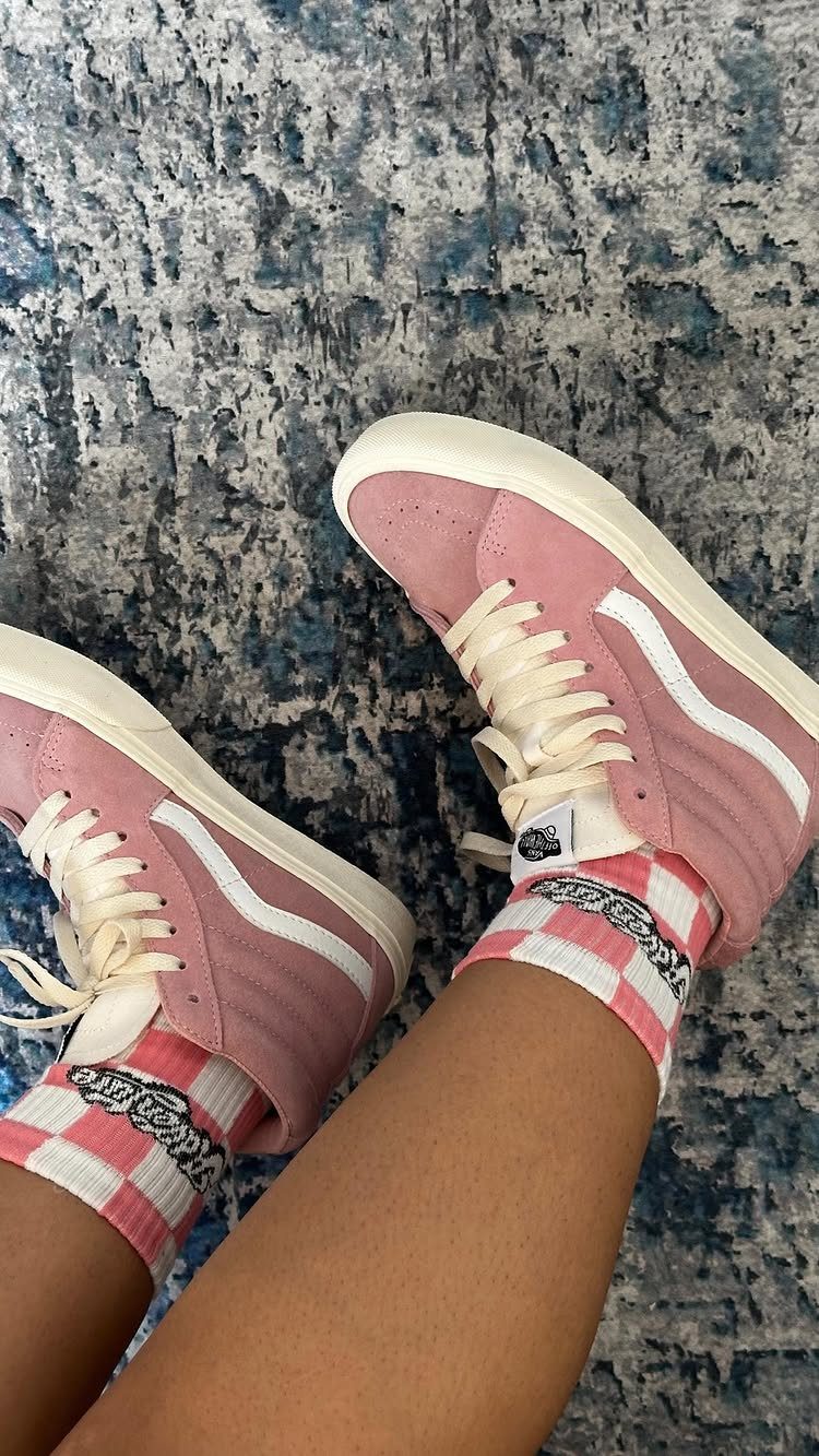 Pink high-top sneakers with white stripes and checkered socks on a blue rug.