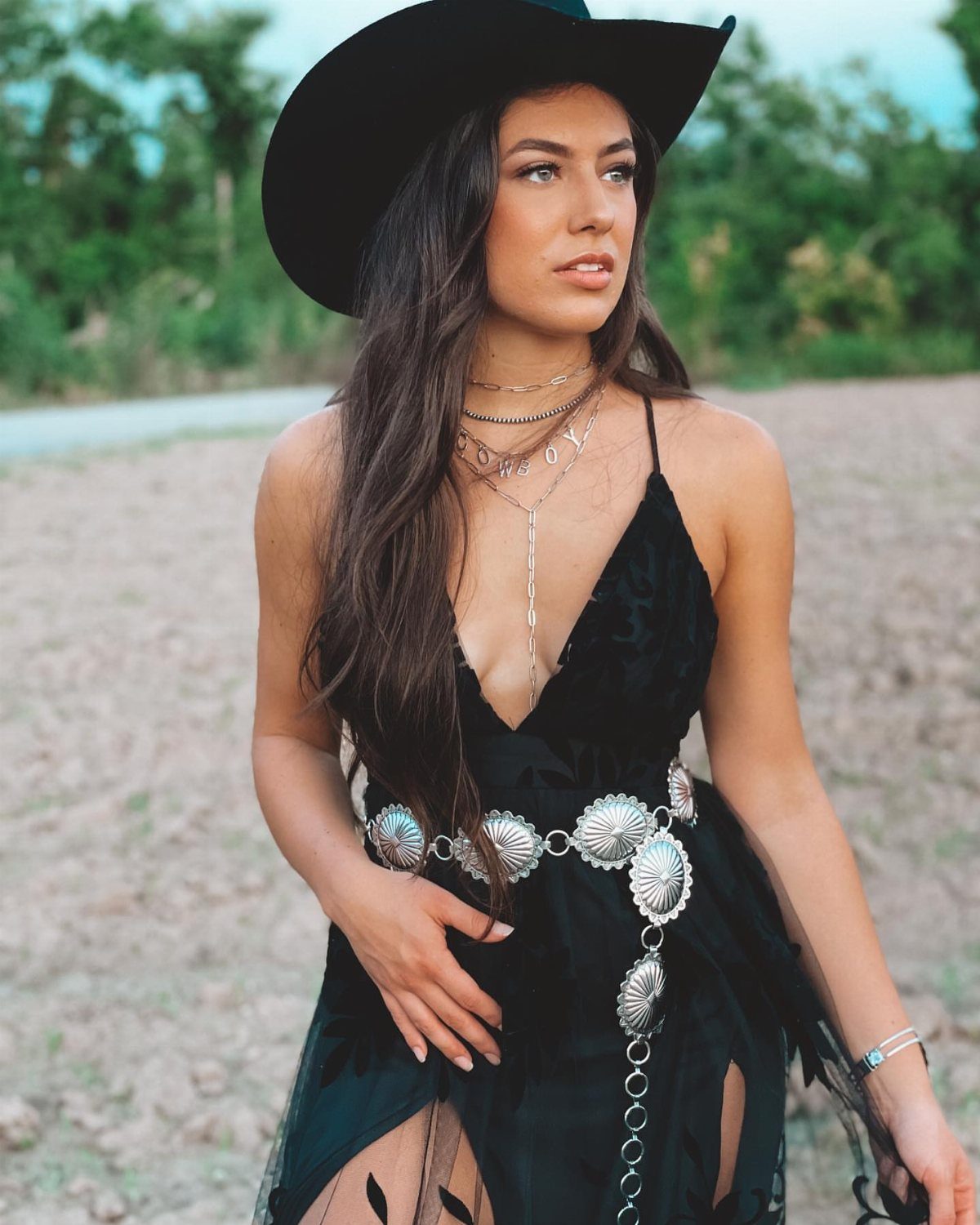 11 Hoedown Outfit Ideas for Boots, Denim and Dresses 7 Woman in black cowboy hat and dress with silver western belt outdoors.