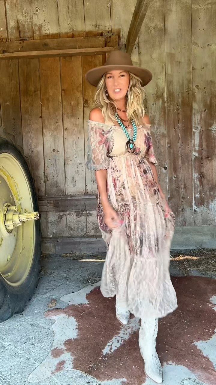 11 Hoedown Outfit Ideas for Boots, Denim and Dresses 2 Woman in a floral maxi dress and brown hat posing by a rustic barn.