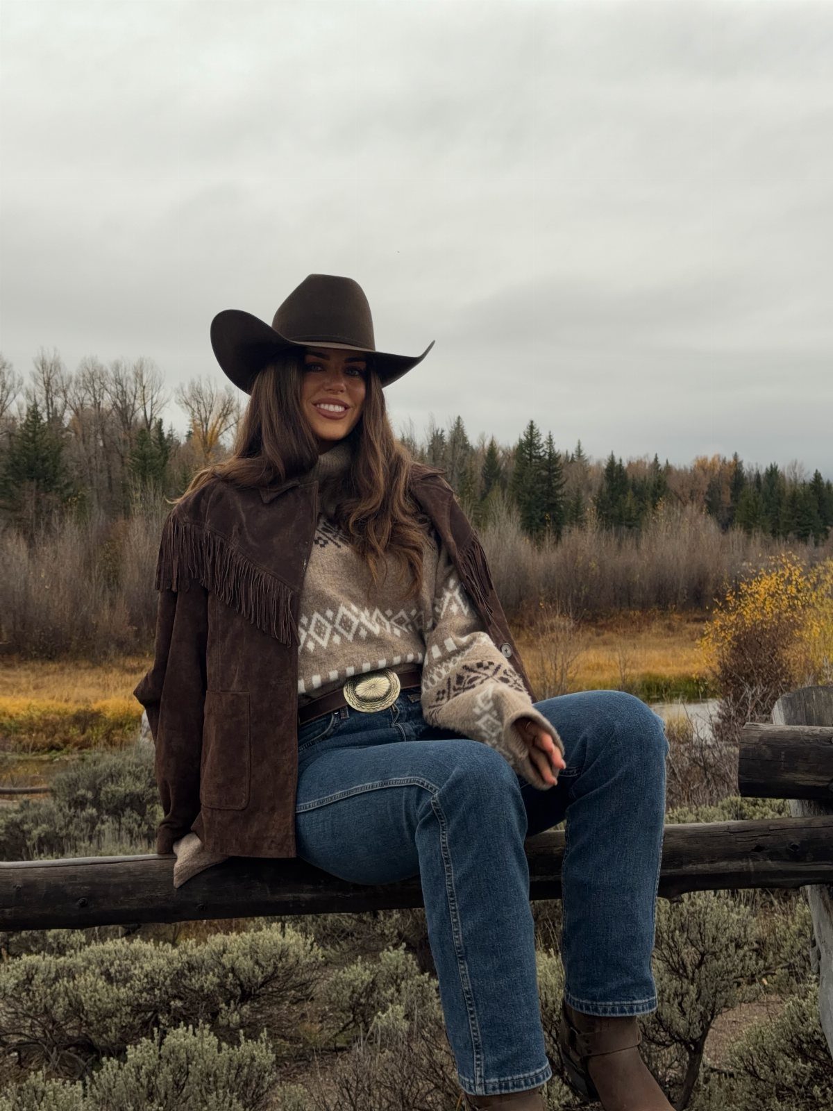 11 Hoedown Outfit Ideas for Boots, Denim and Dresses 6 Woman in cowboy hat, fringed suede jacket, and jeans sitting on wooden fence.