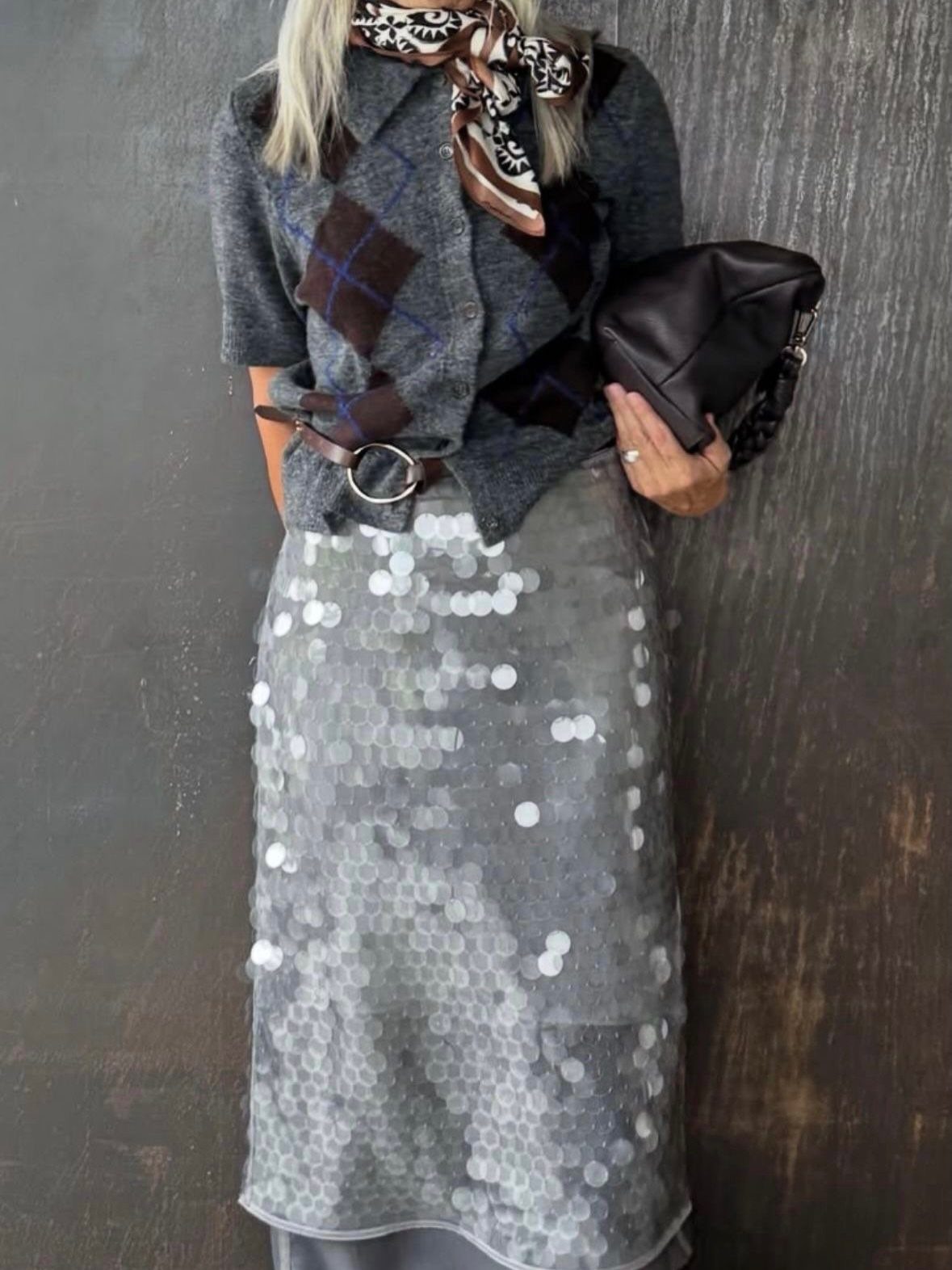 8 Holiday Party Attire for Women to Wear This Season 2 Woman wearing a grey argyle sweater and a shimmering silver sequined midi skirt.