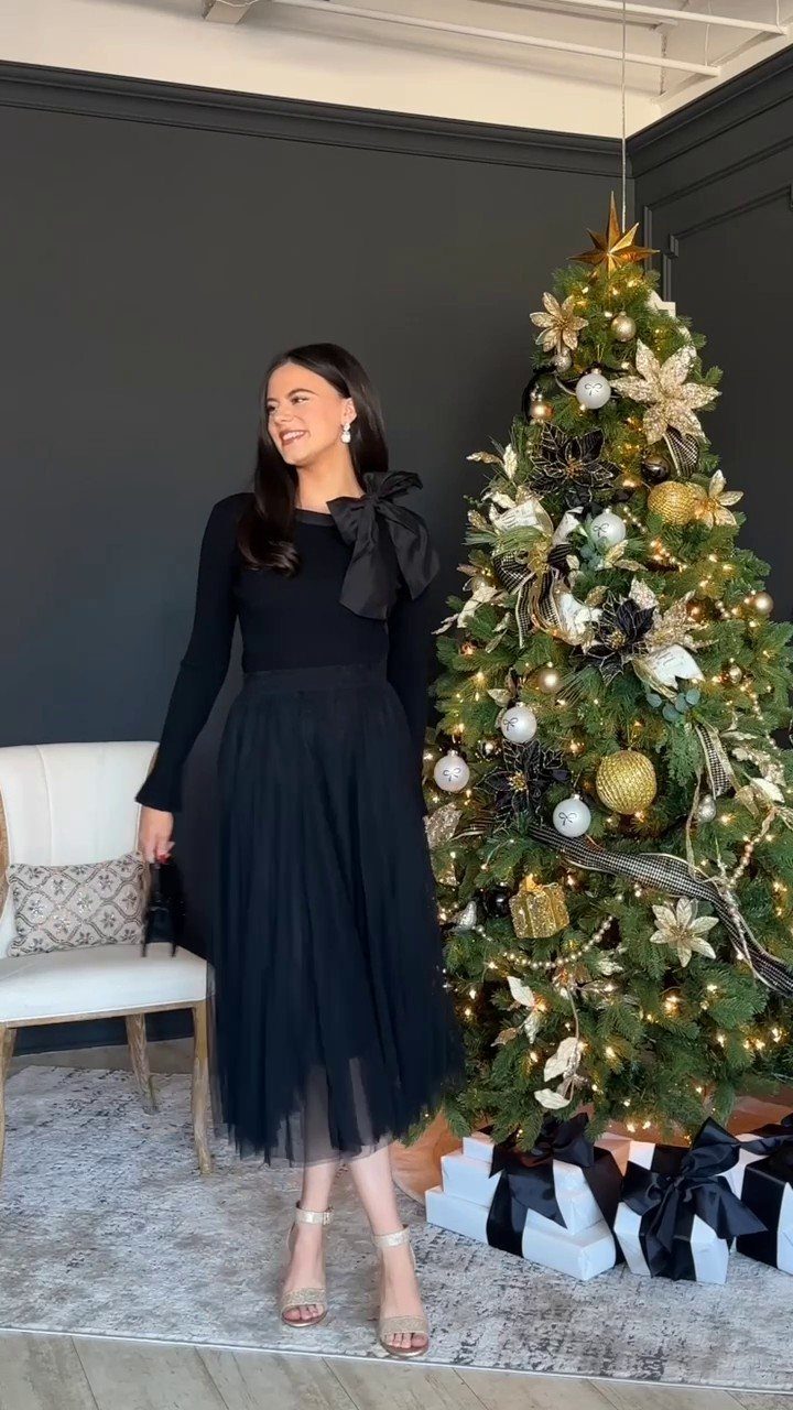8 Holiday Party Attire for Women to Wear This Season 4 Woman in black bow blouse and tulle skirt standing by a Christmas tree