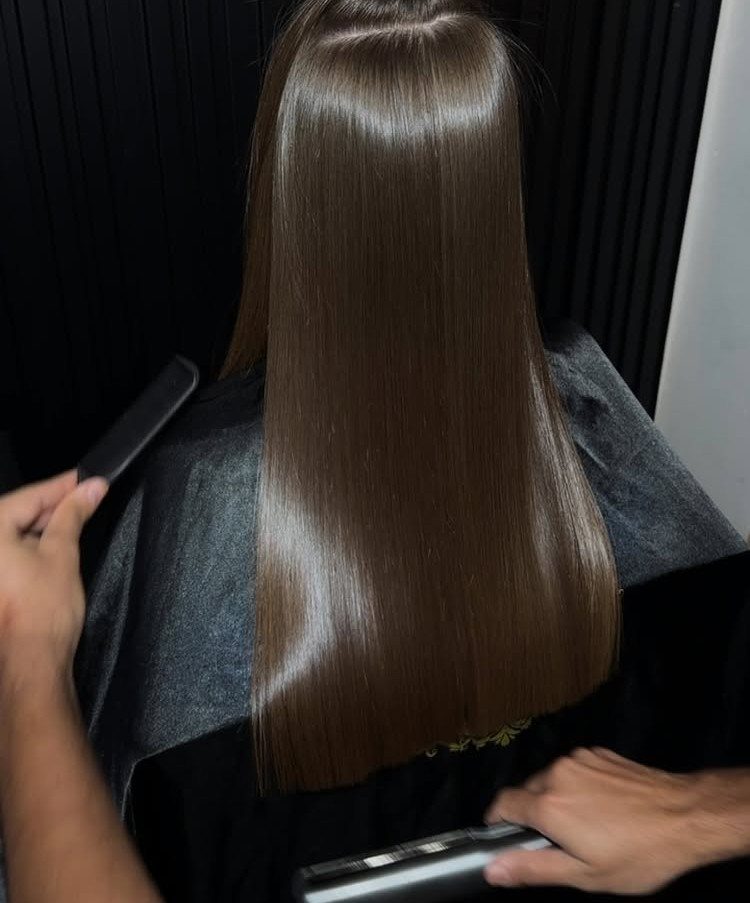 Korean Glass Hair: 6 Sleek and Shiny Styles to Try 1 Shiny straight brown hair being styled with a flat iron in a salon