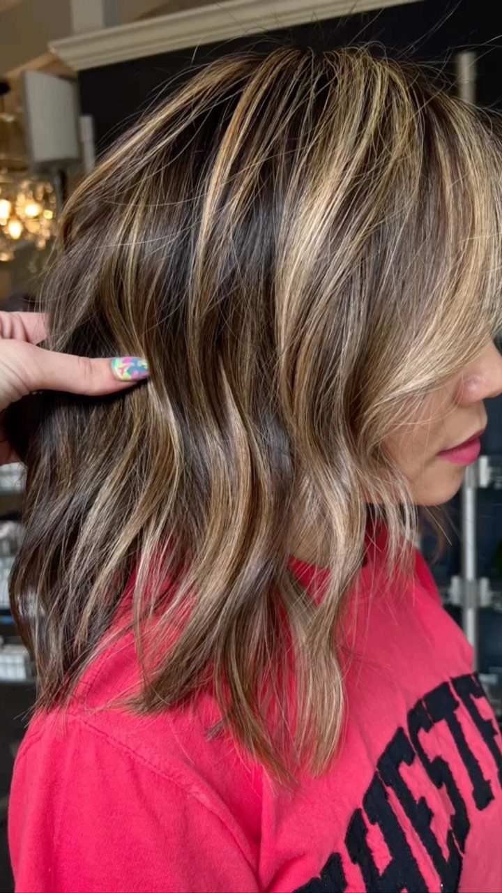 Level 2 Hair Ideas: 5 Looks for Dark Brown Bases 4 Woman with dark brown hair and blonde highlights in a salon setting.