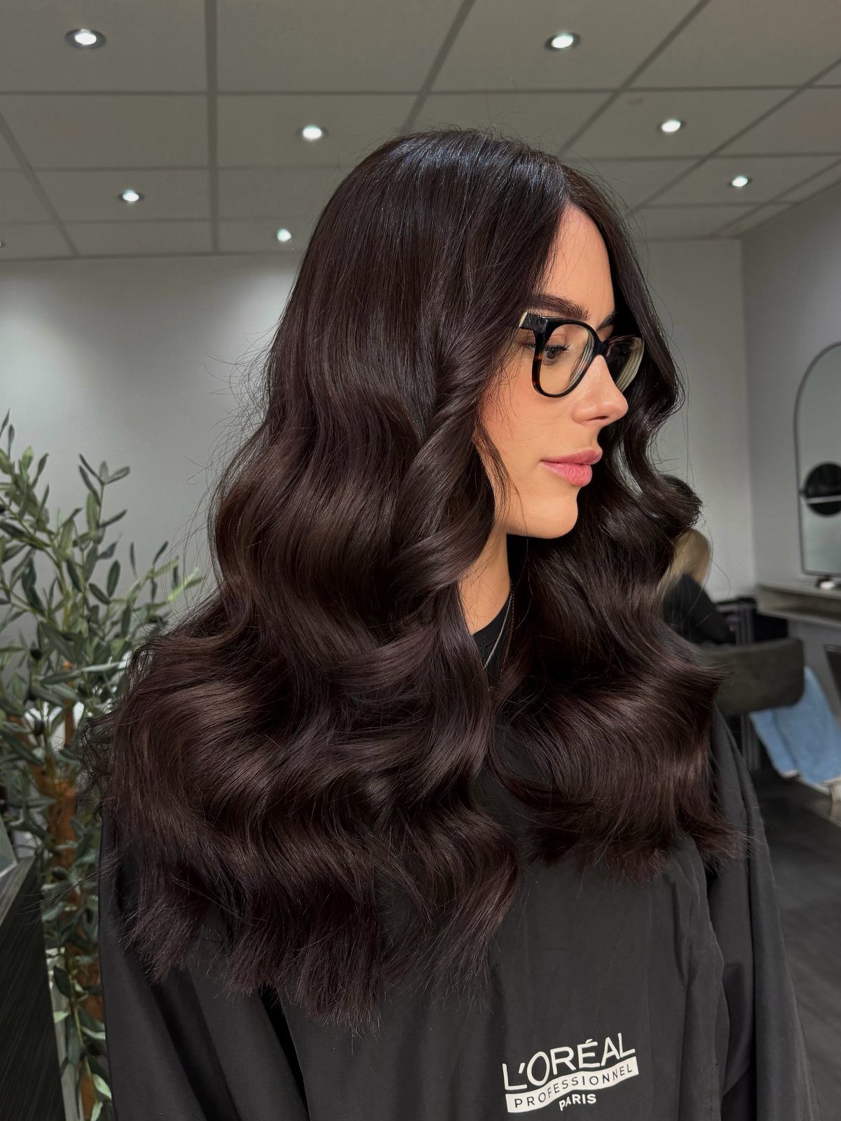 Level 2 Hair Ideas: 5 Looks for Dark Brown Bases 3 Woman with long, wavy, dark brown hair wearing black glasses in a salon