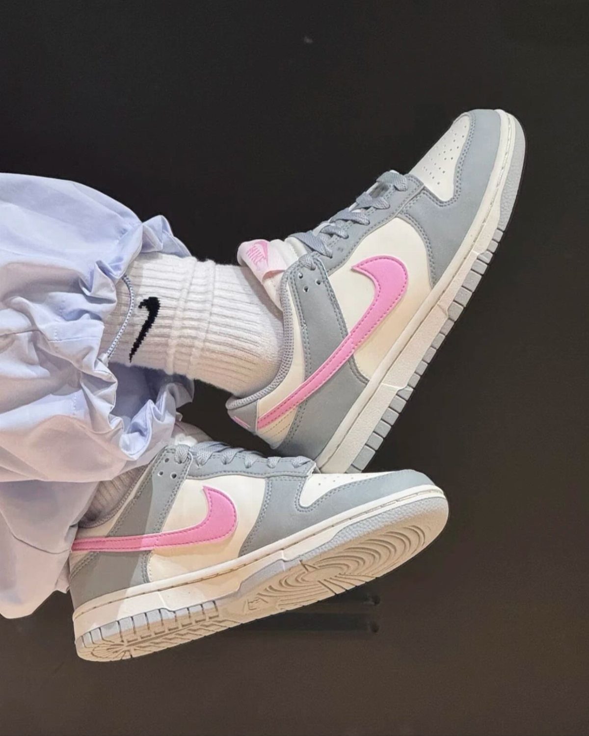 Light Grey Dunks: 5 Ideas, From Smoke Grey to Gum Soles 4 Light grey Nike Dunk sneakers with pink swooshes and white socks.