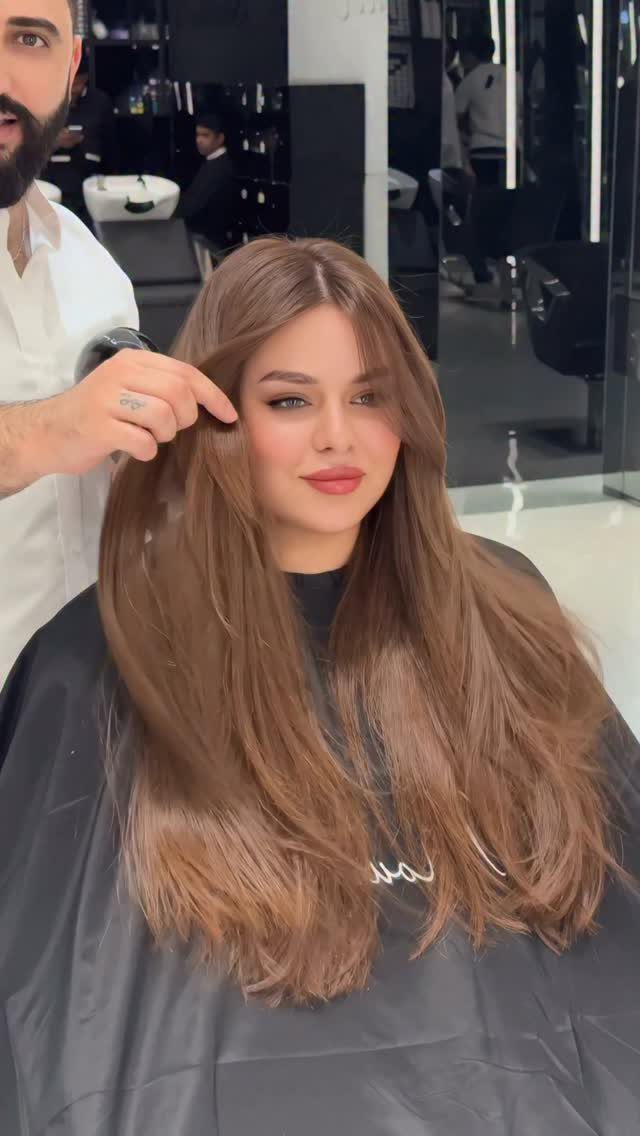 Woman with long layered brown hair and curtain bangs in a hair salon