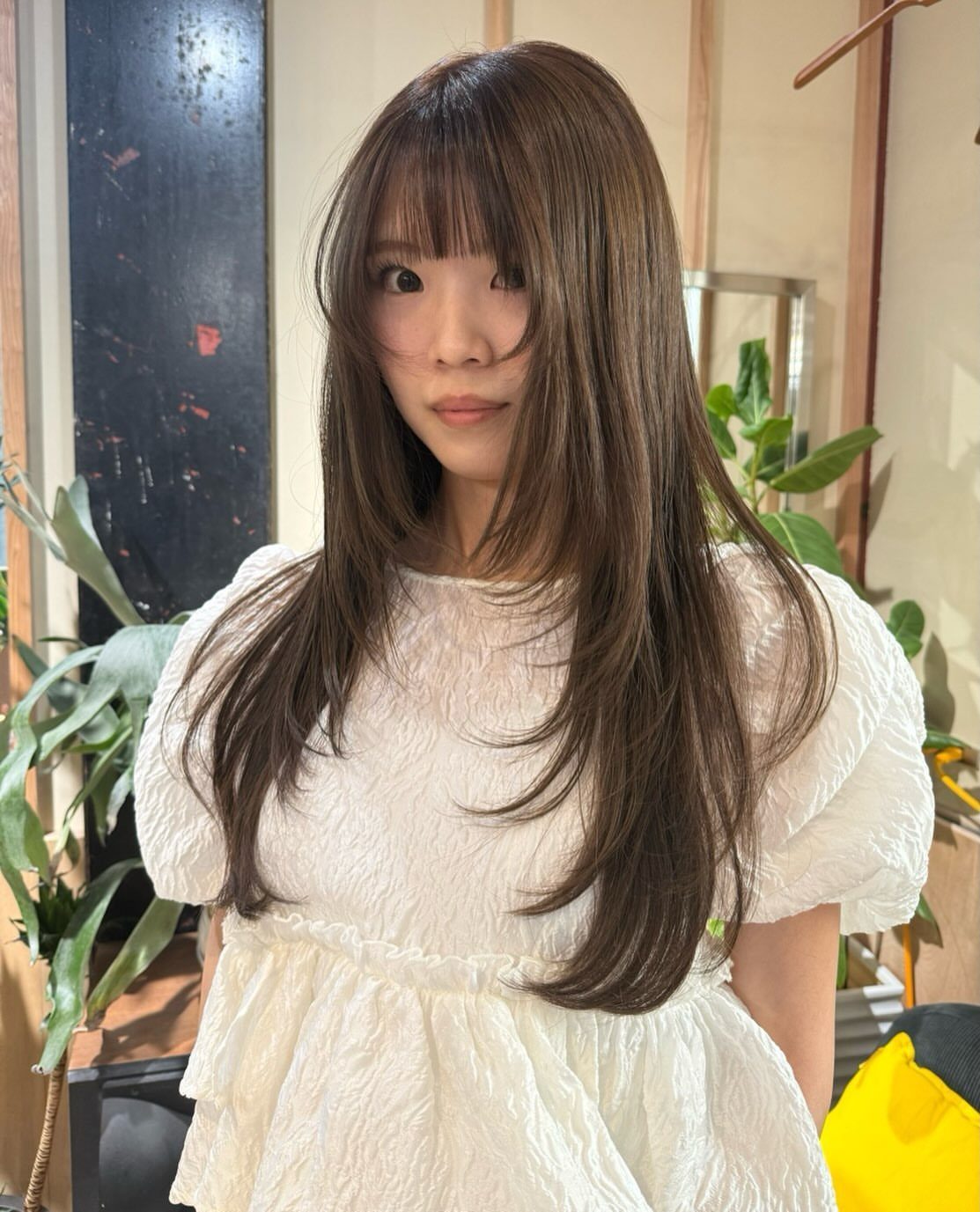 Woman with long brown hair and wispy bangs wearing a white dress.
