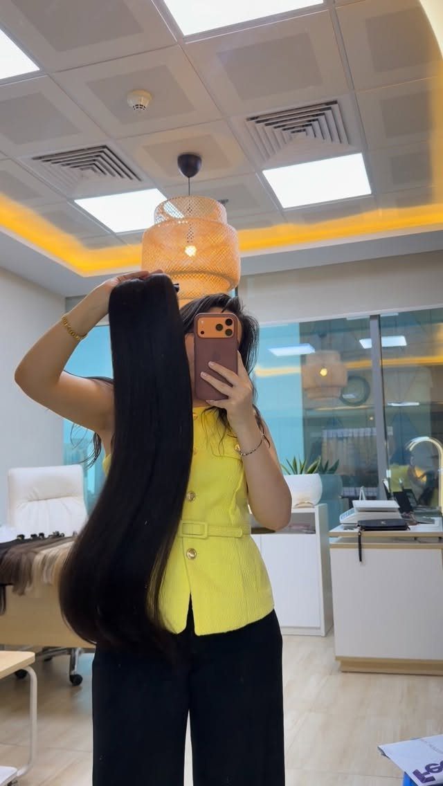 Long Russian Hair Ideas: 8 Looks, Colors and Textures 1 Woman in yellow vest holding long, silky dark brown hair in a salon