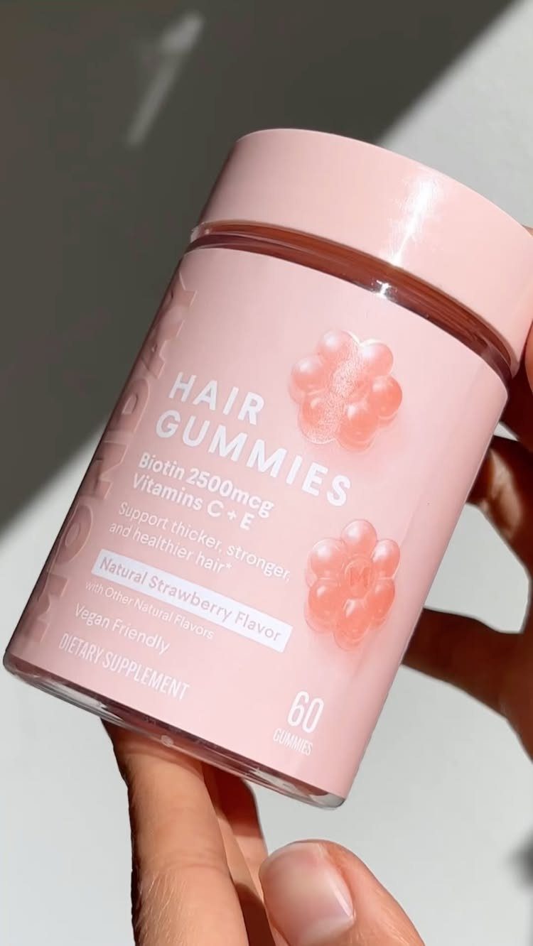 7 Ways to Make Hair Grow Faster, From Biotin to Microneedling 1 Pink bottle of biotin hair gummies held by a person's hand.