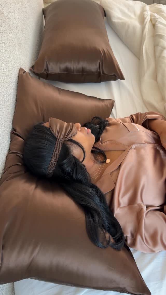 7 Ways to Make Hair Grow Faster, From Biotin to Microneedling 2 Woman with long dark hair resting on a brown satin pillowcase in bed.