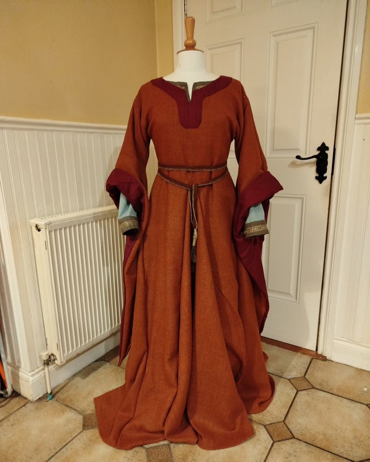 Rust-colored medieval bliaut gown with flared sleeves on a white mannequin.