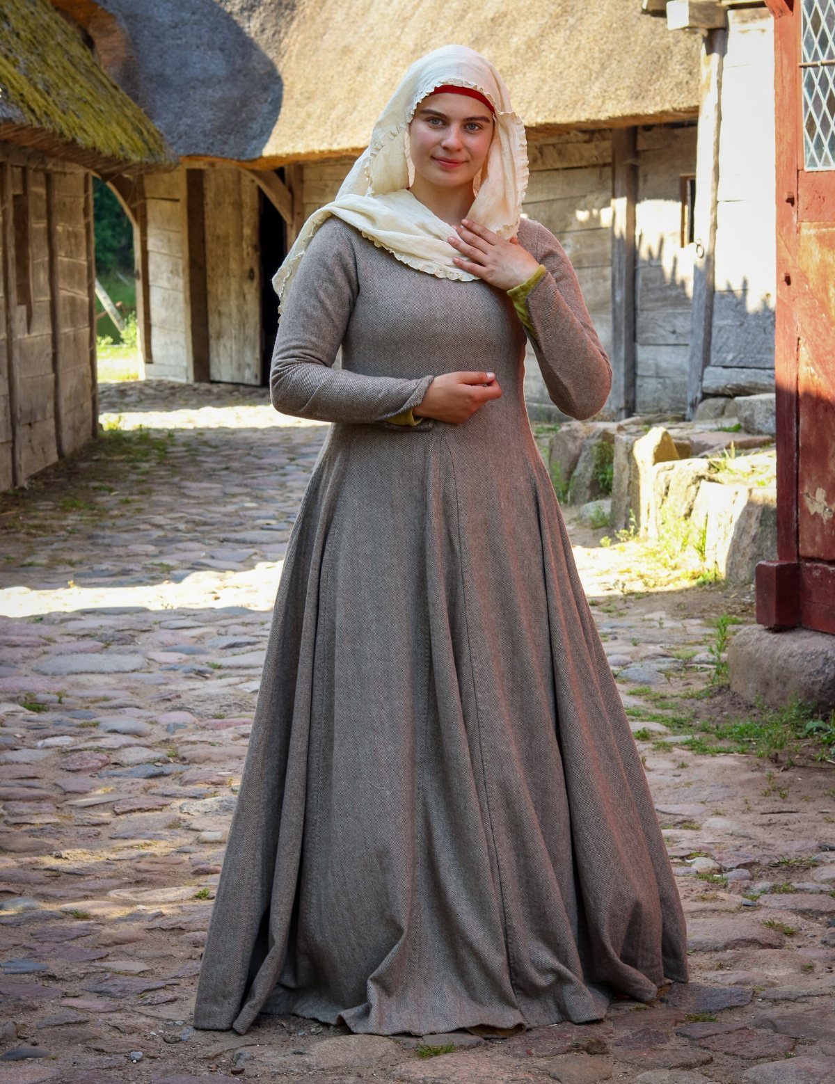 Woman in a brown floor-length medieval cotte and white veil on cobblestone street