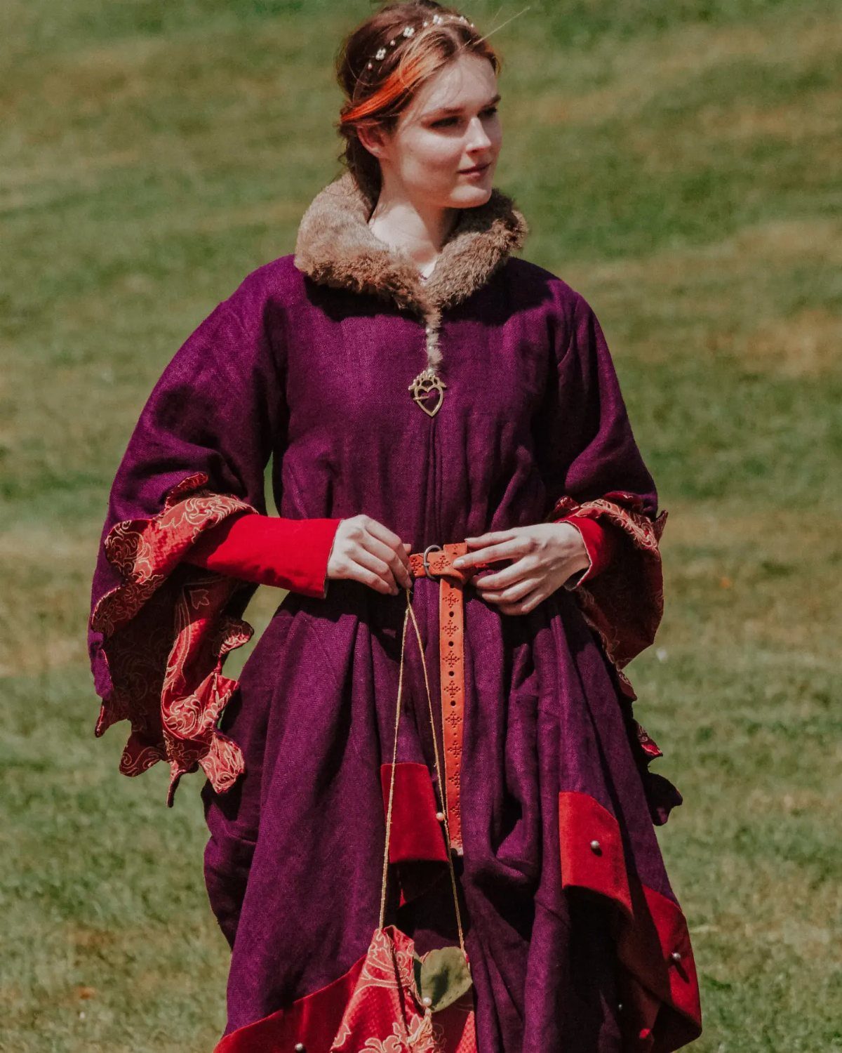 Woman in a voluminous purple houppelande gown with fur collar in a field