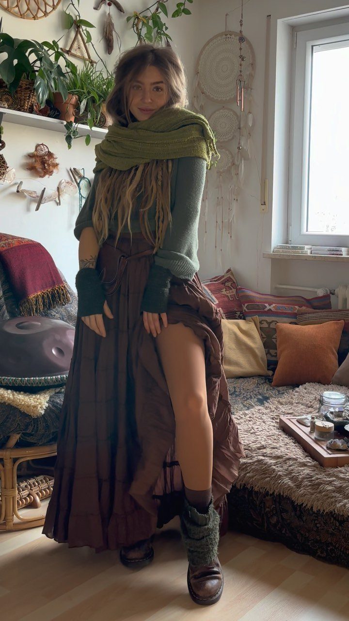 Woman wearing layered green top, scarf, and brown skirt in a bohemian room.