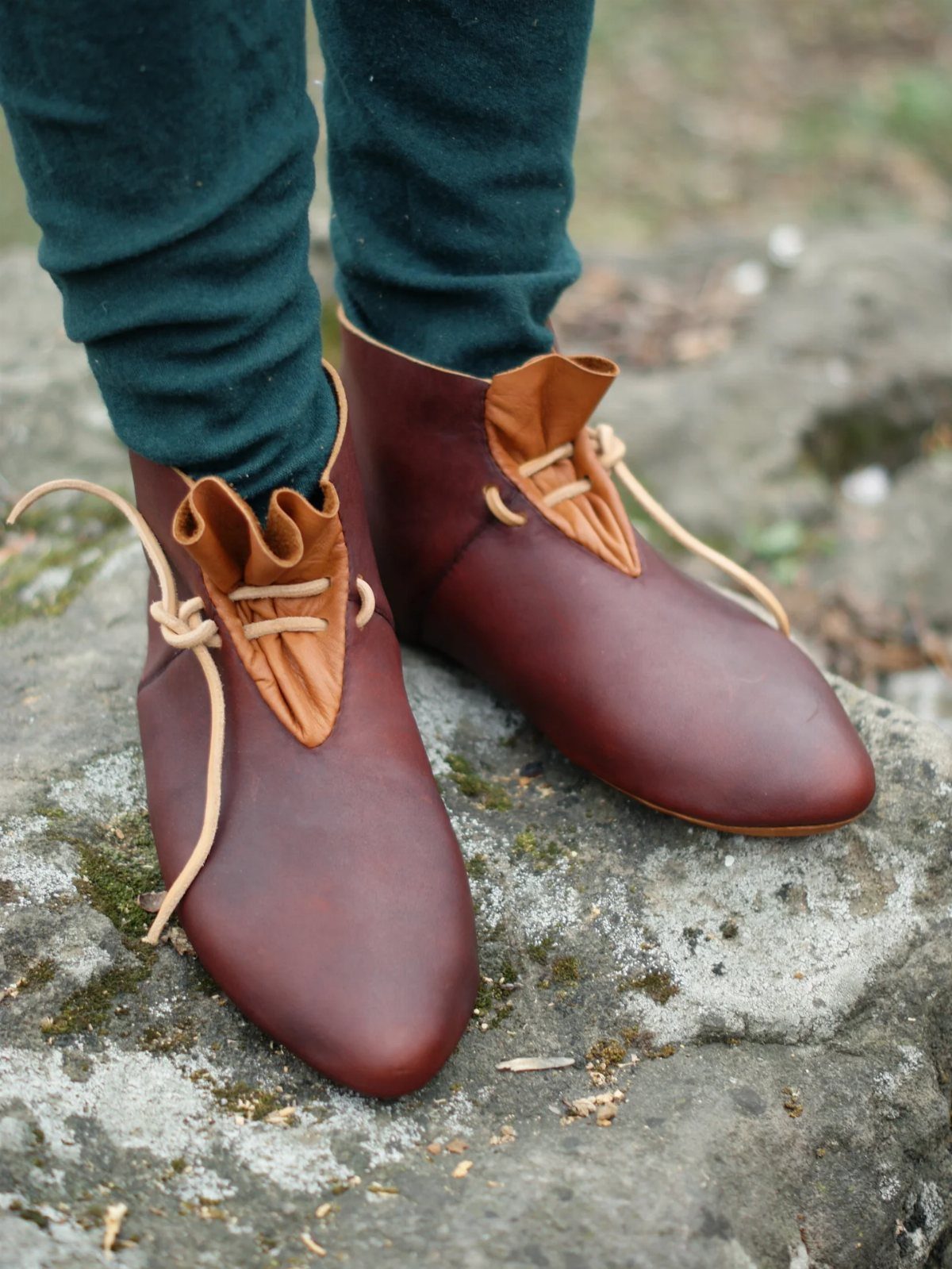 Brown leather medieval shoes with laces worn on a grey stone surface