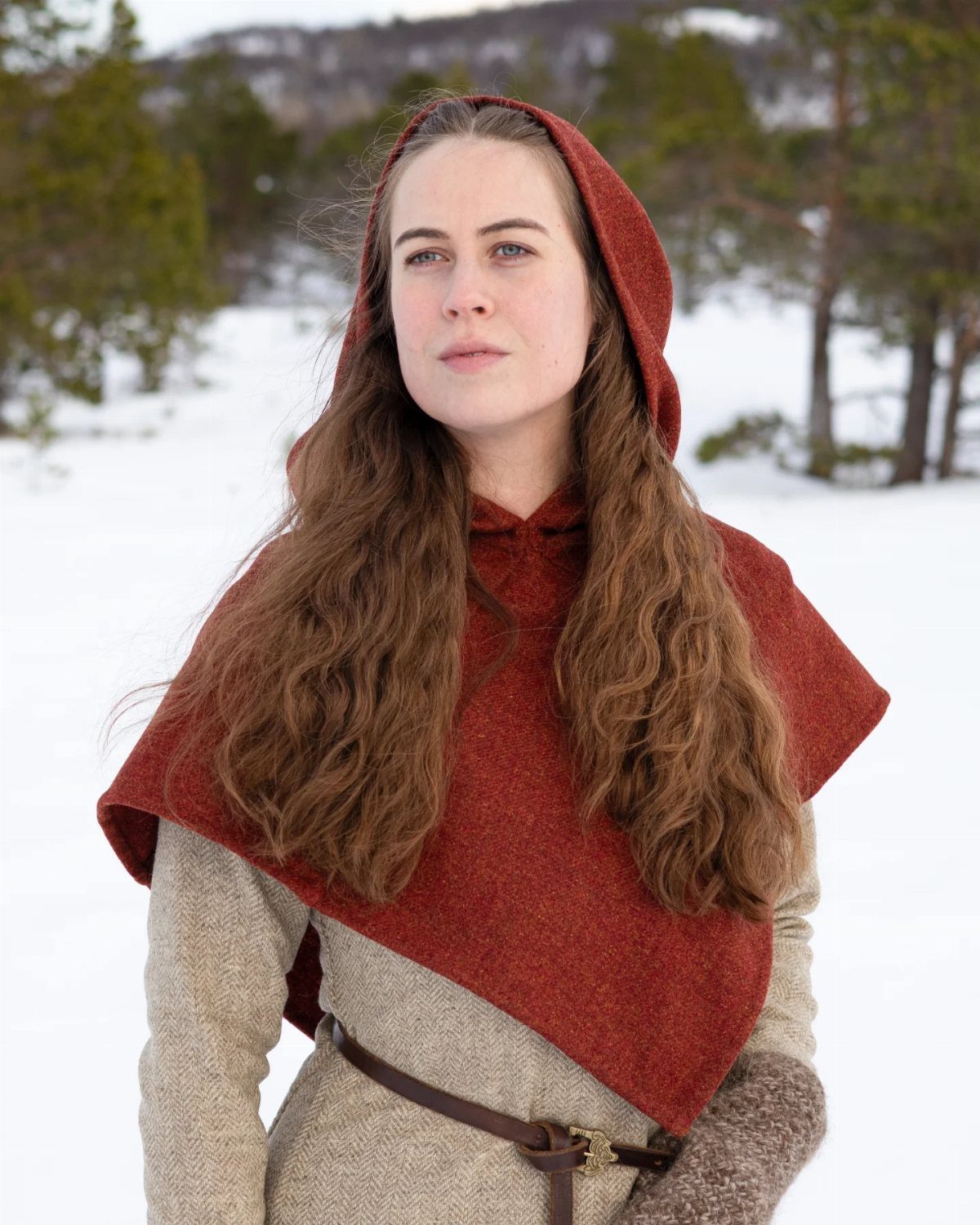 Woman wearing a reddish-brown wool hood and cape in a snowy forest setting