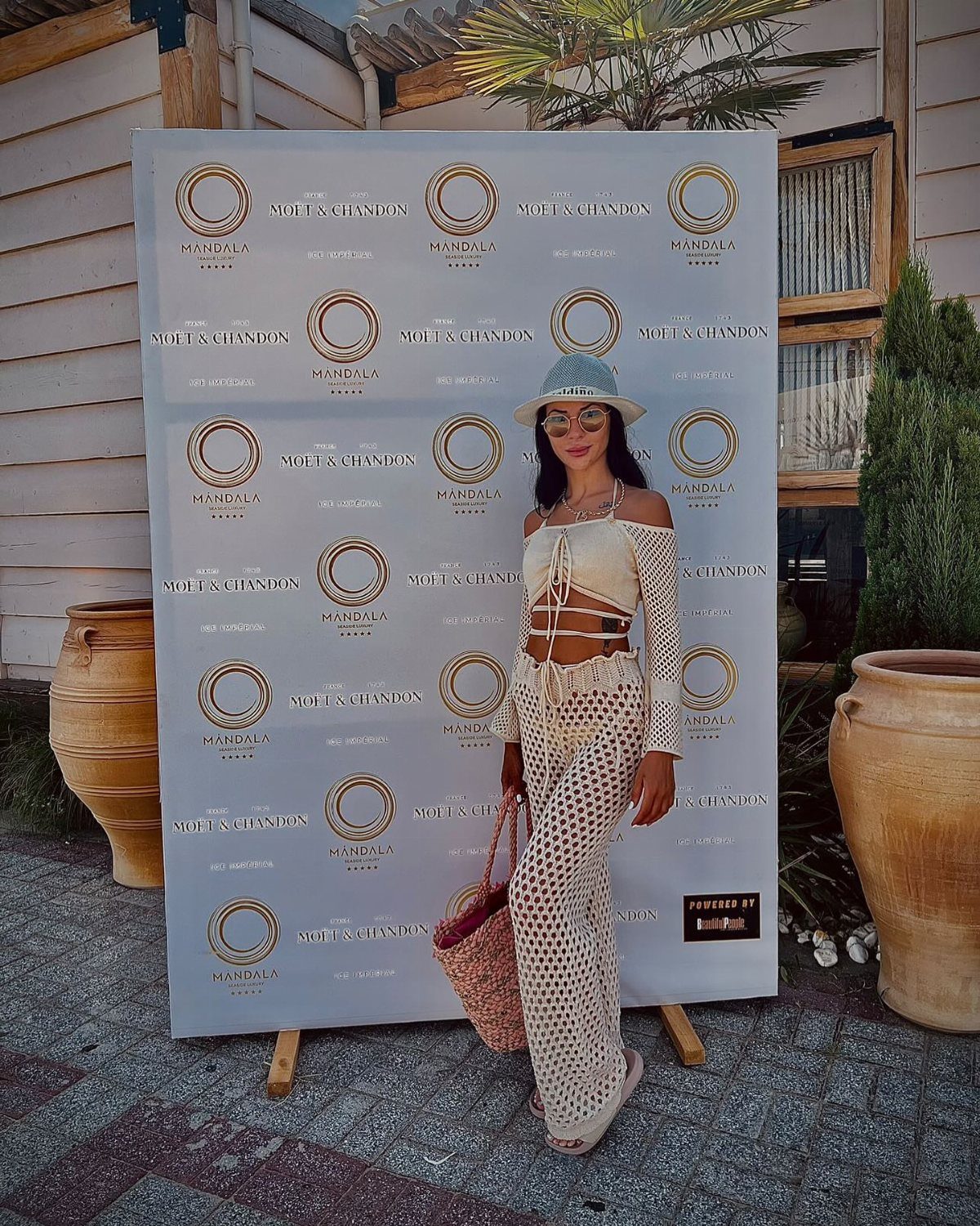Miami Club Outfits: 8 Ideas for Day and Night 5 Woman in cream crochet outfit and blue sun hat posing by branded backdrop