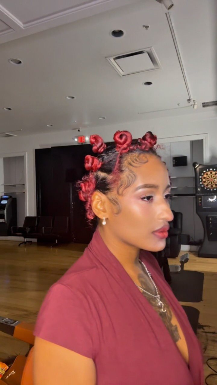 Woman with red natural hair styled in Bantu knots wearing a maroon top.