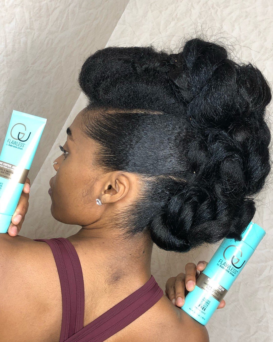 Woman with a voluminous black faux bun holding light blue hair product bottles.