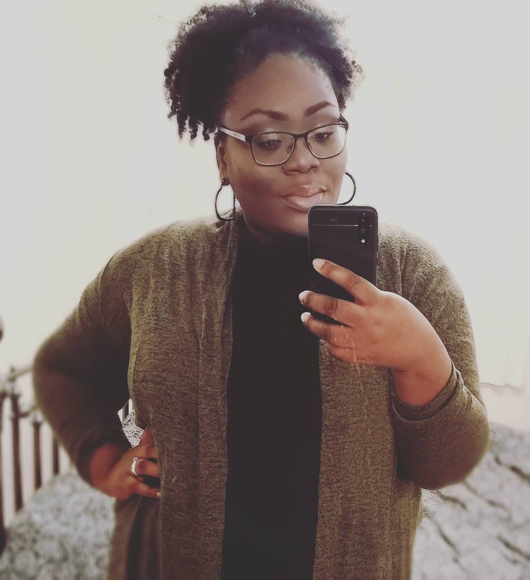 Woman with natural hair styled in a high puff taking a mirror selfie.