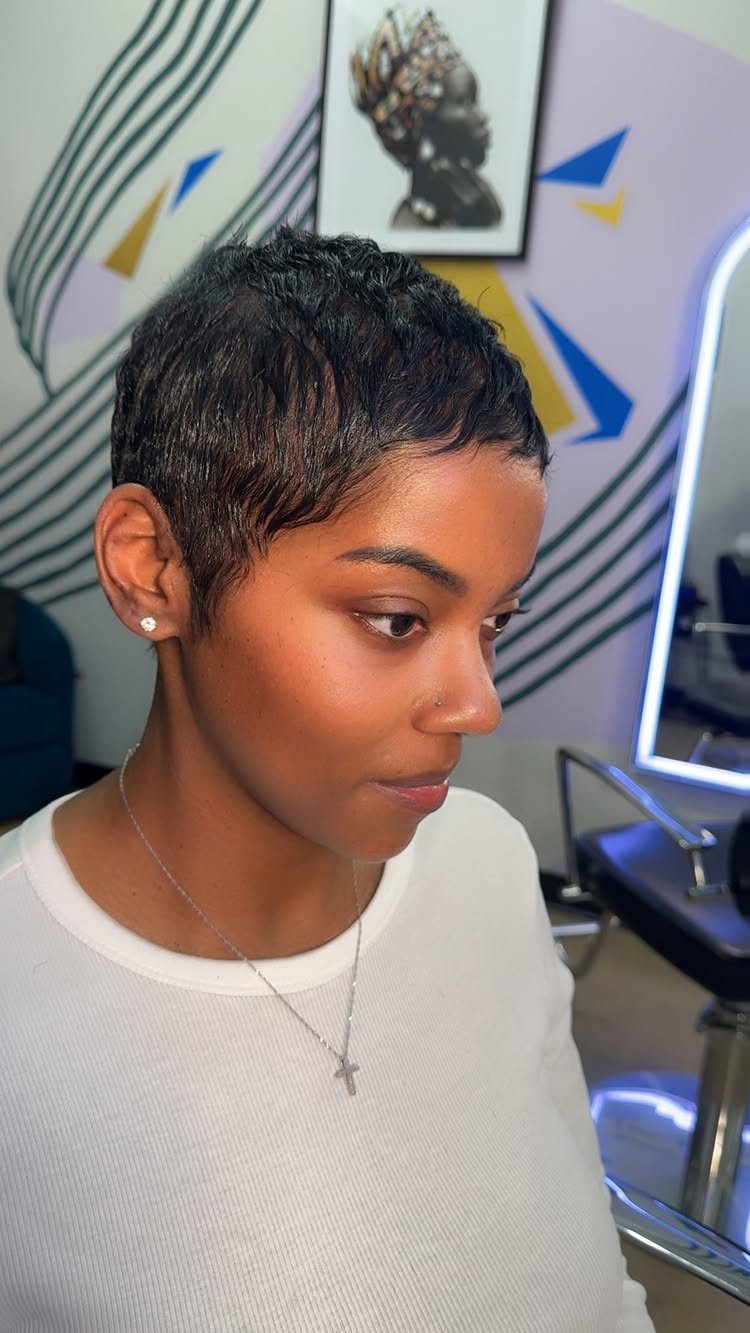 Woman with short, dark textured natural hair wearing a white shirt and necklace.