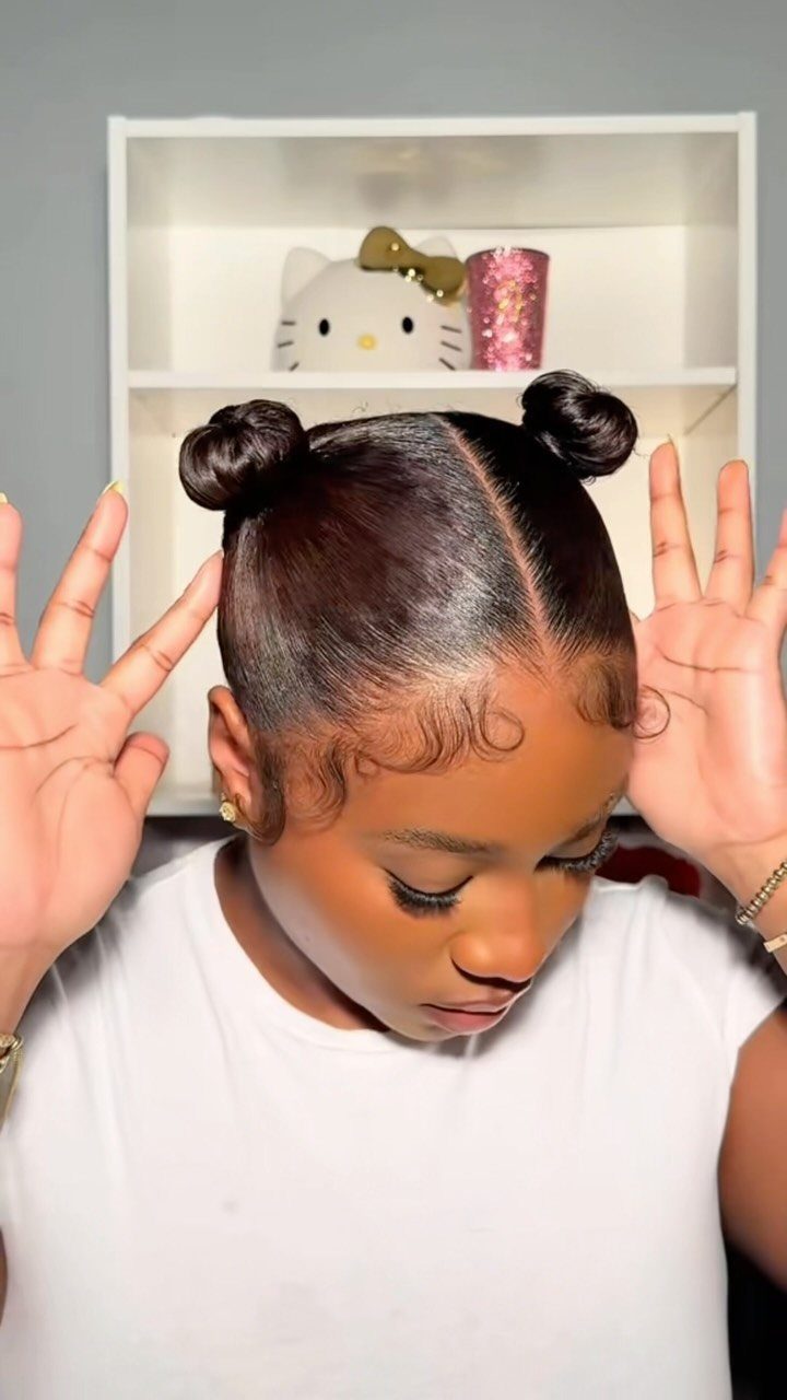 Woman with dark hair styled in two space buns and curled edges.