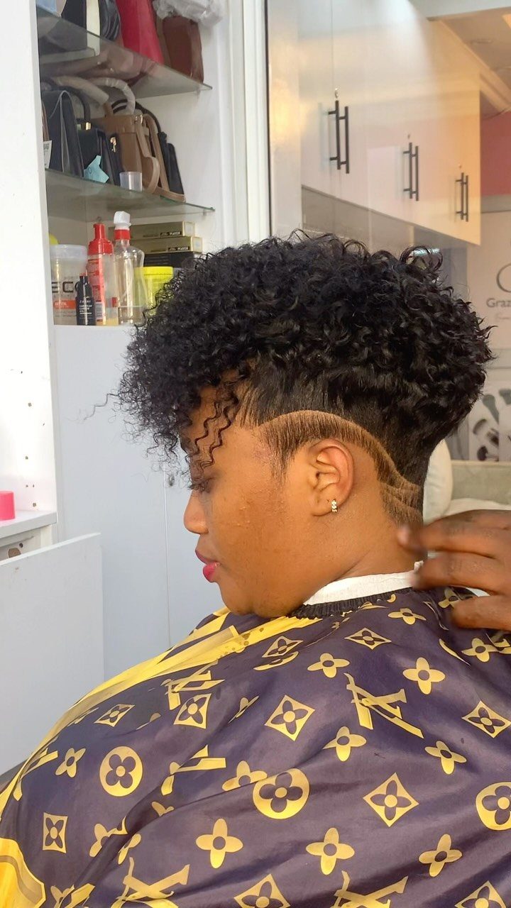 Person with a taper fade and natural curls wearing a patterned salon cape.