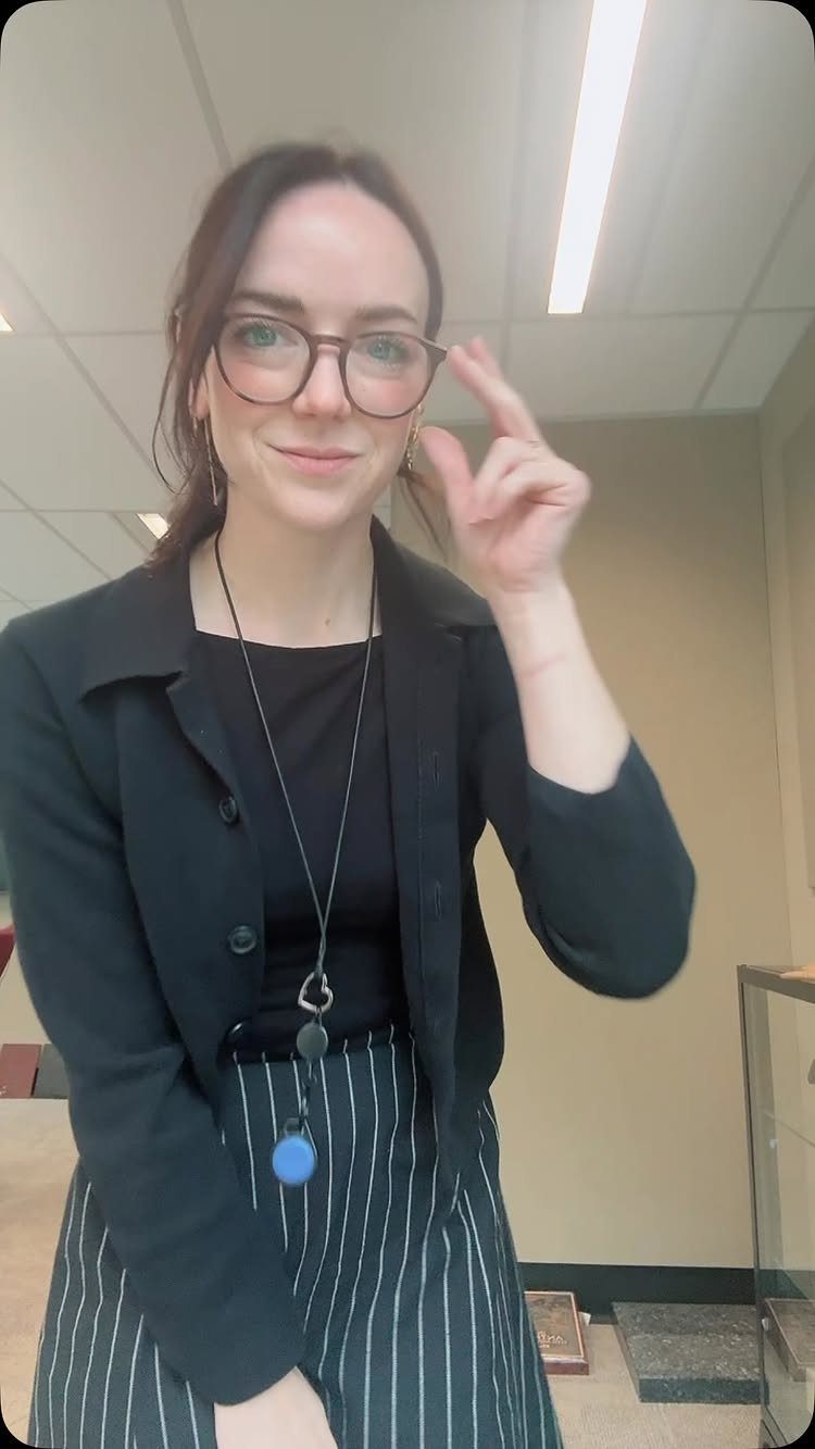 Woman wearing a black blazer and pinstriped pants in an office setting.
