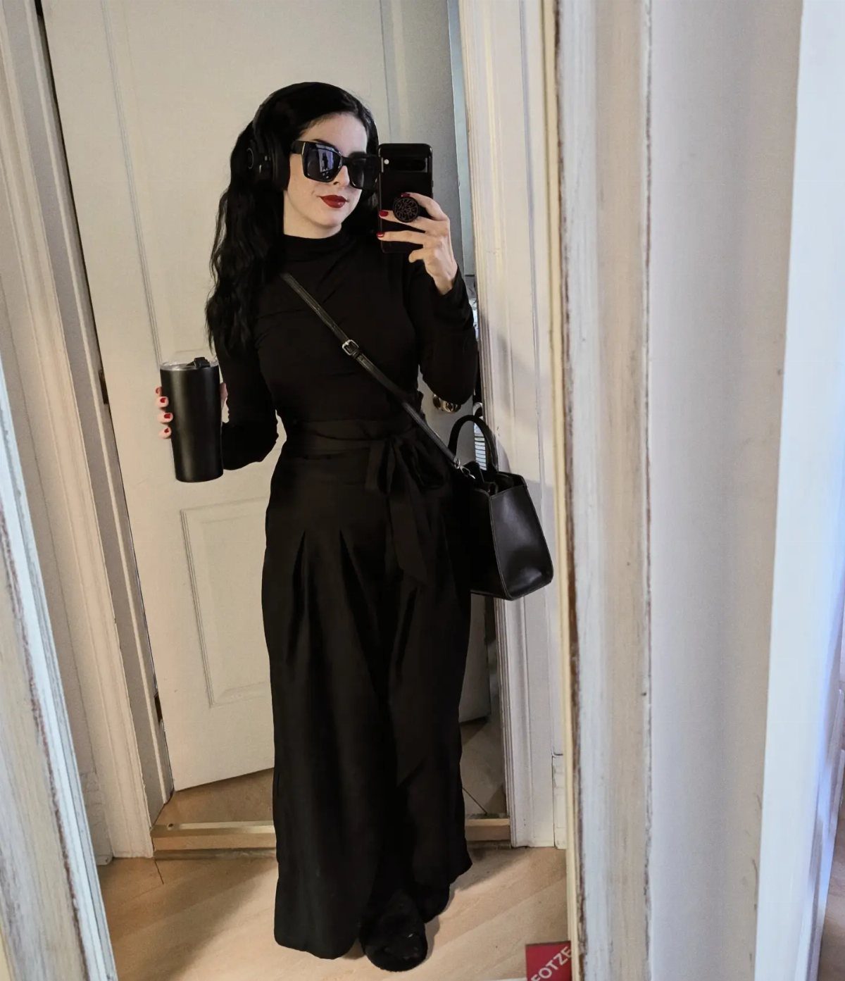 Person in all-black office goth outfit with wide-leg trousers and black sunglasses.