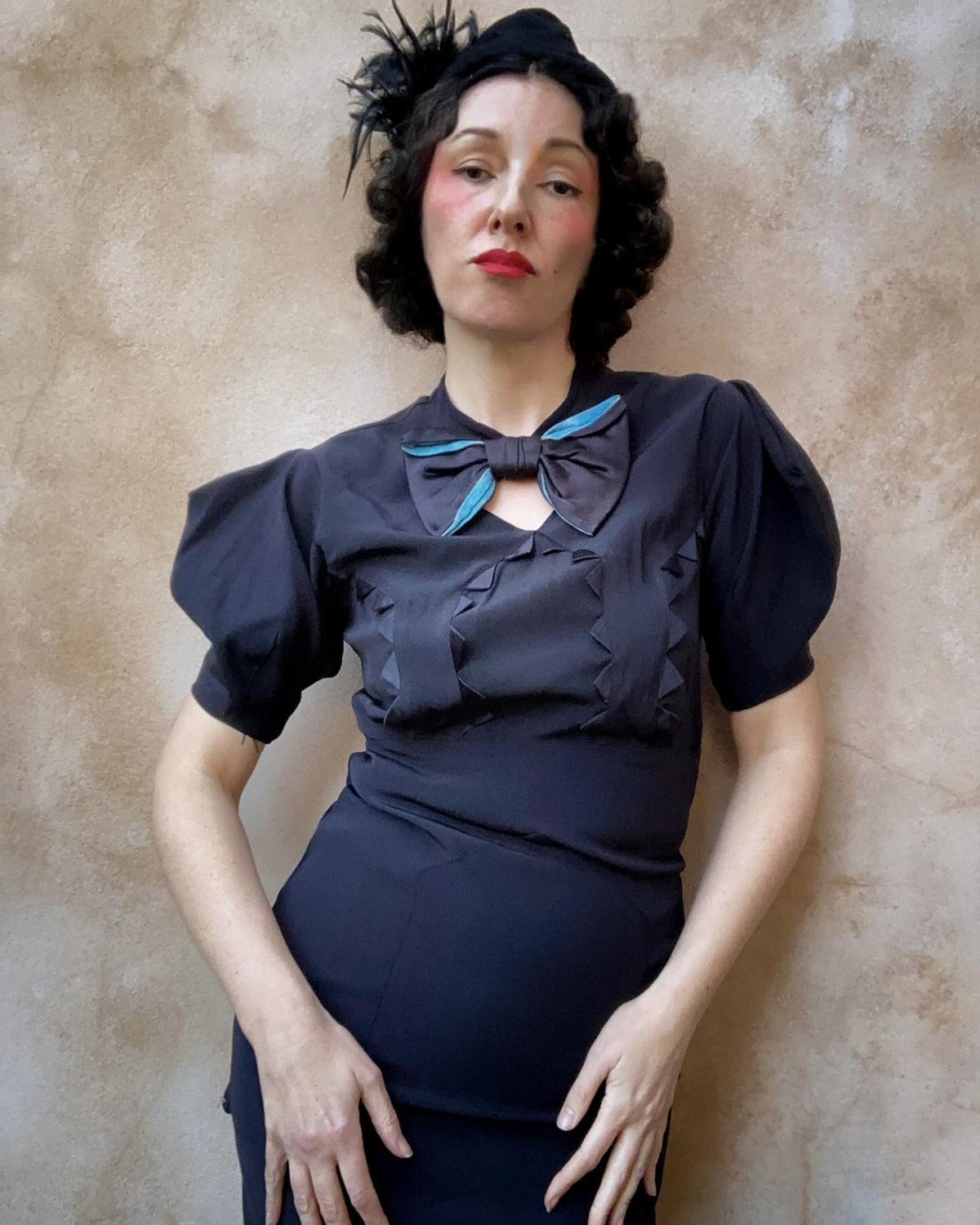 Woman in a vintage black dress with puffed sleeves and a blue bow.