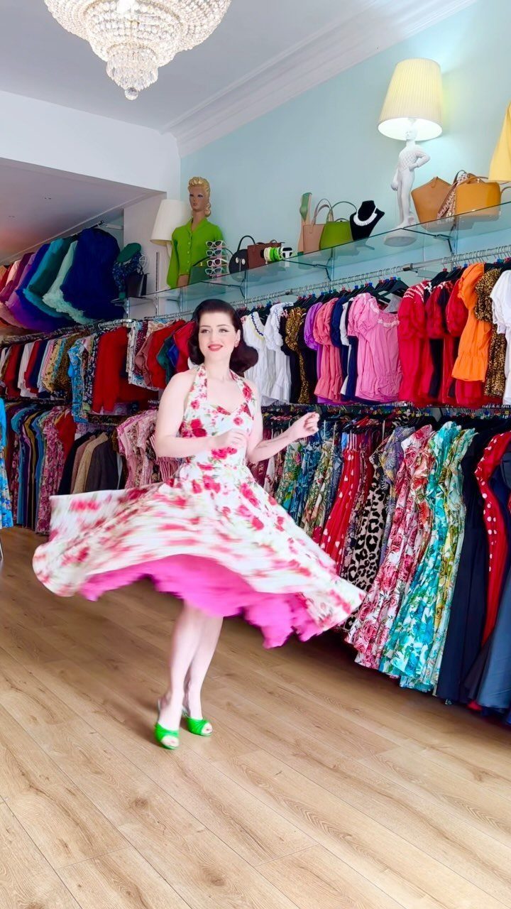Woman spinning in a pink floral swing dress inside a vintage clothing boutique.