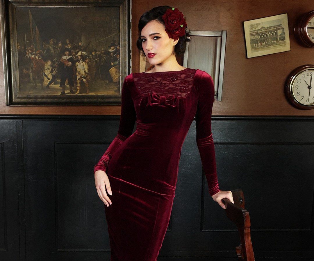 Woman in a burgundy velvet midi dress with lace neckline and red hair flower.