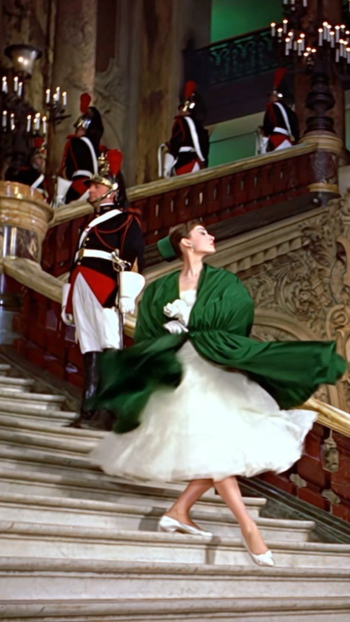 Audrey Hepburn in a white dress and green wrap on a grand staircase