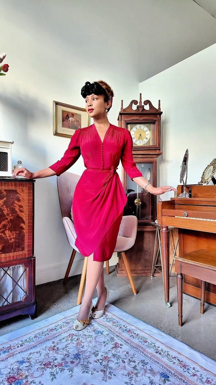 Woman in a fitted red vintage-style dress posing in a classic interior room.