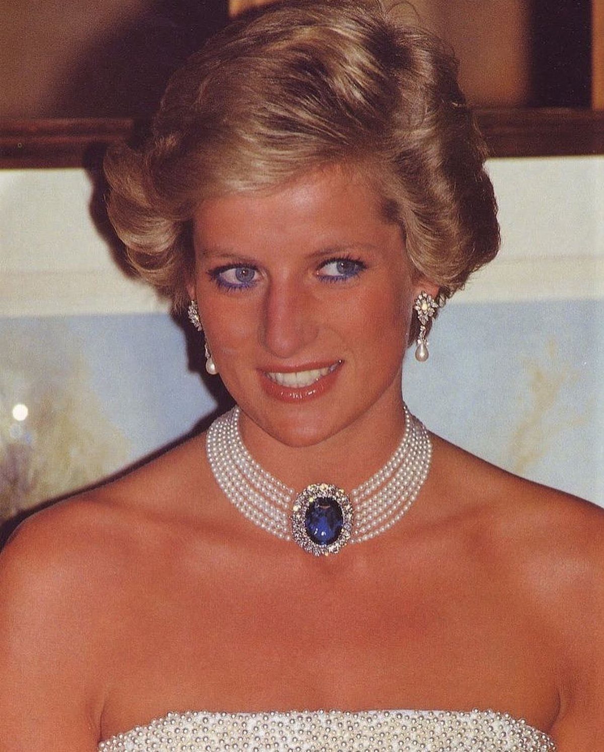 Woman wearing a multi-strand pearl choker with a blue gemstone and pearl earrings.