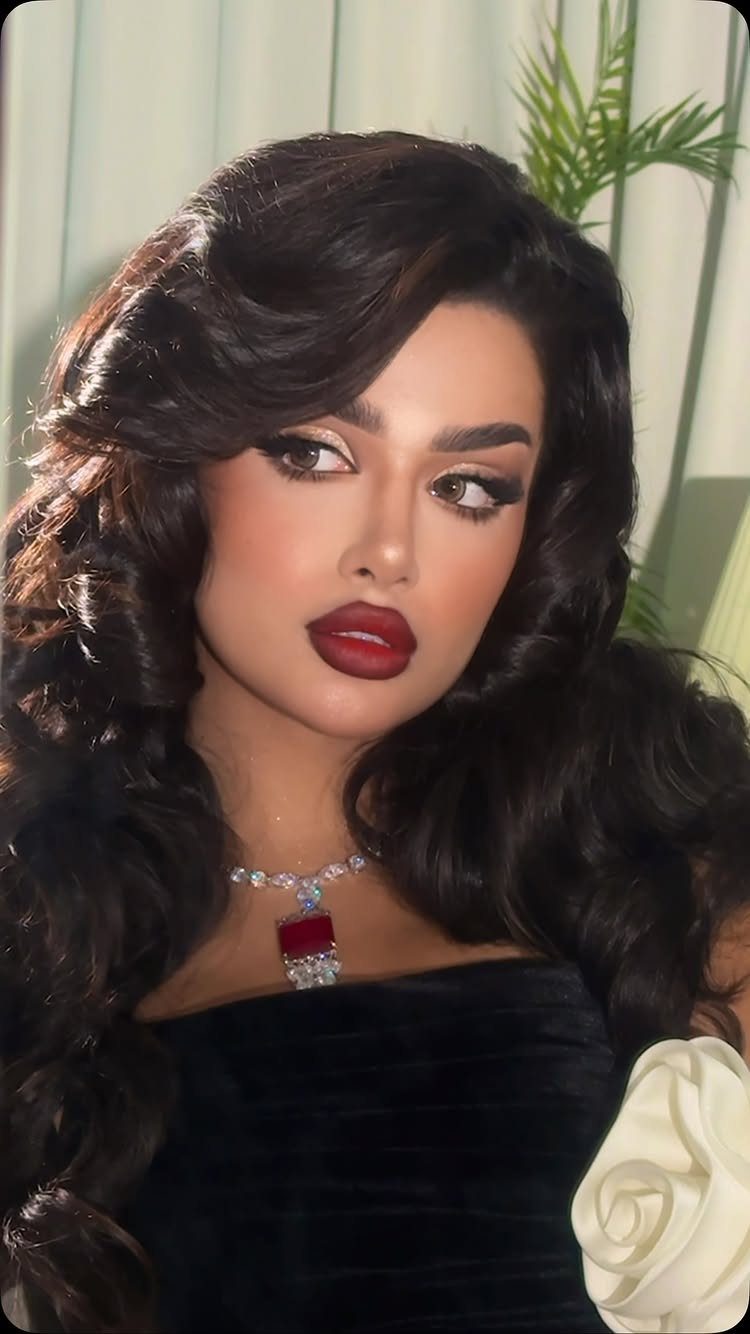 Woman with voluminous dark waves and bold red lipstick wearing a black dress.