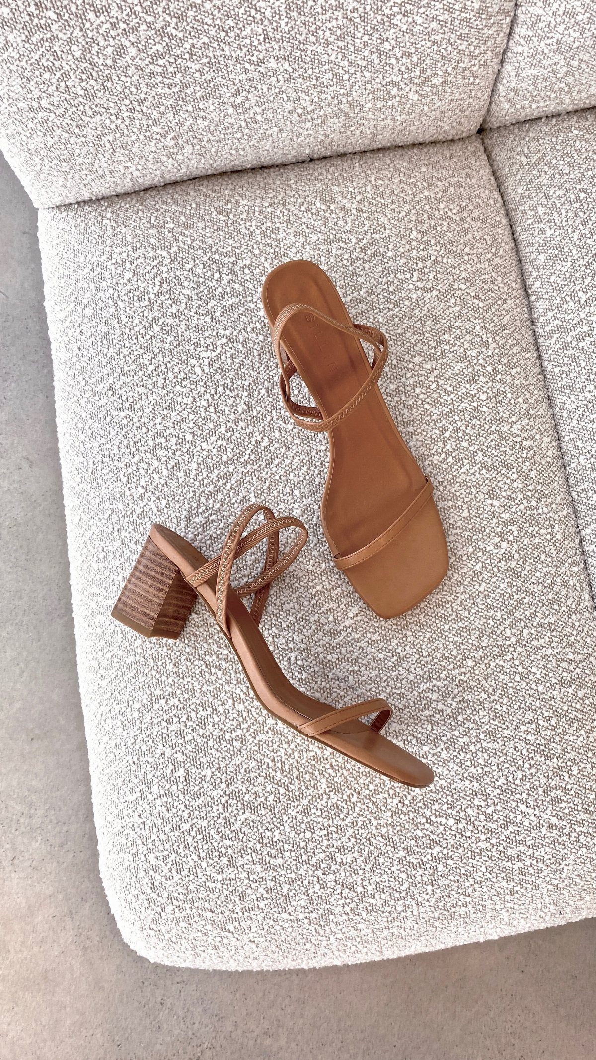 Brown leather strappy sandals with block heels on a white boucle fabric surface.