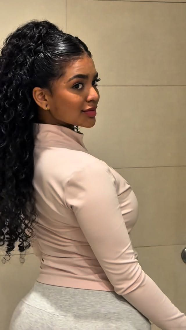 11 Peinado Pelo Rizado Ideas for Every Curl Type 1 Woman with dark curly hair styled in a high ponytail wearing pink top.