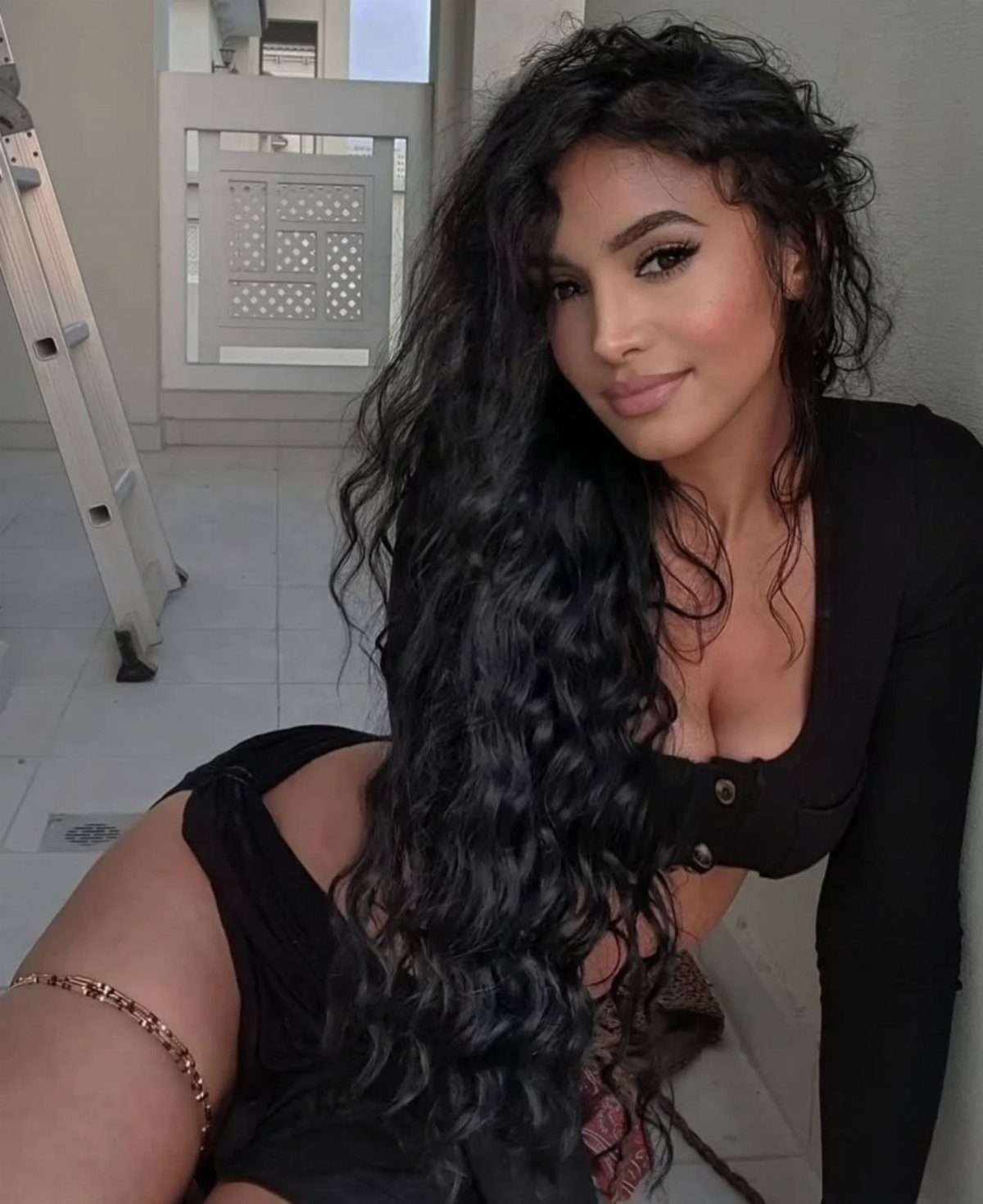 11 Peinado Pelo Rizado Ideas for Every Curl Type 7 Woman with long voluminous dark curly hair wearing a black top posing indoors.