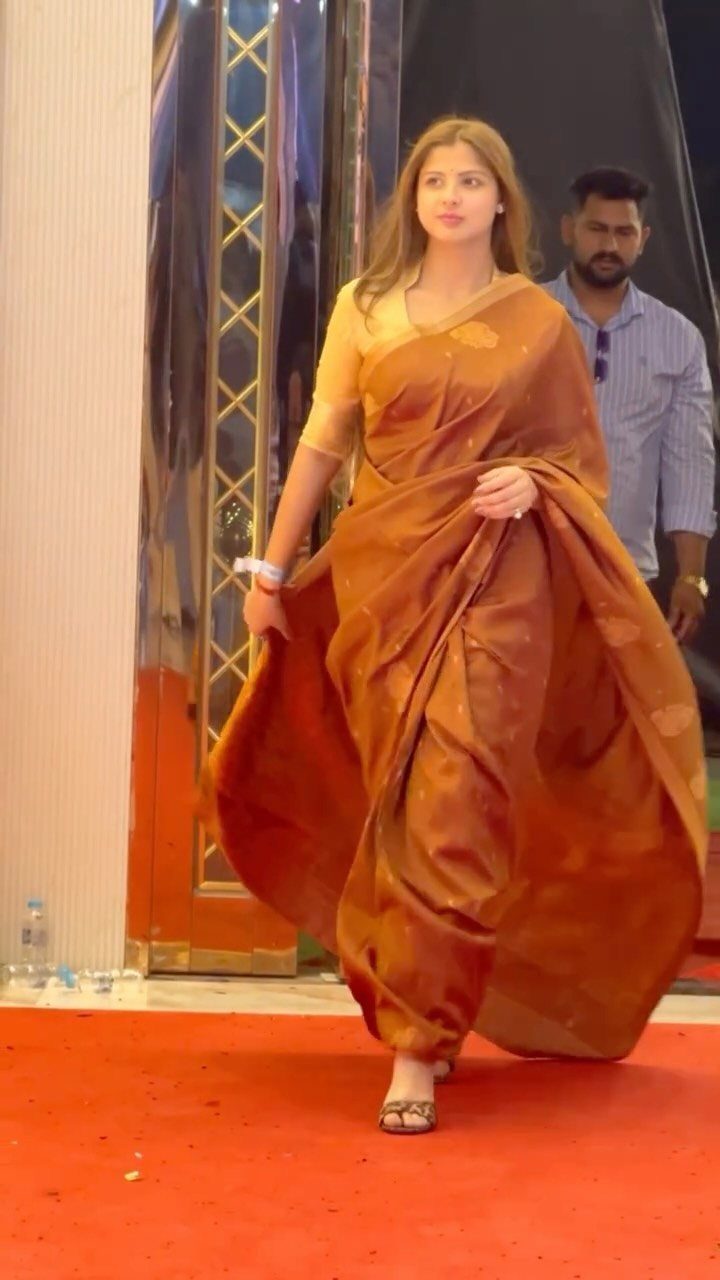 Woman in a gold-orange saree walking on a red carpet at an event.