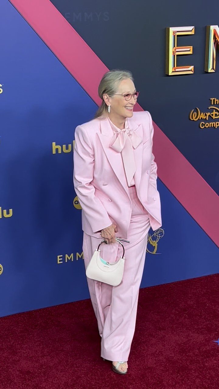 Woman in a light pink suit and bow tie posing on red carpet.