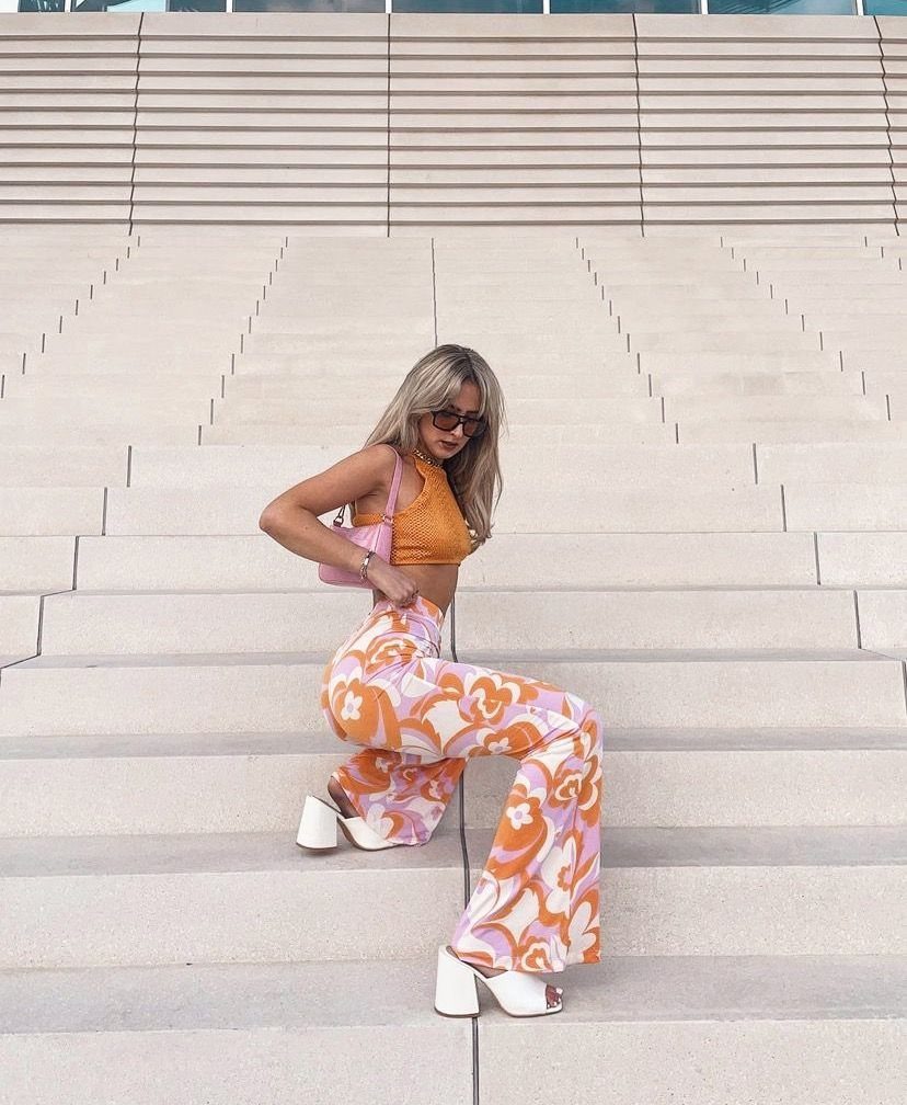 6 Retro Bell Bottoms Ideas for Every Closet and Mood 5 Woman in floral bell bottoms and orange crop top posing on concrete steps