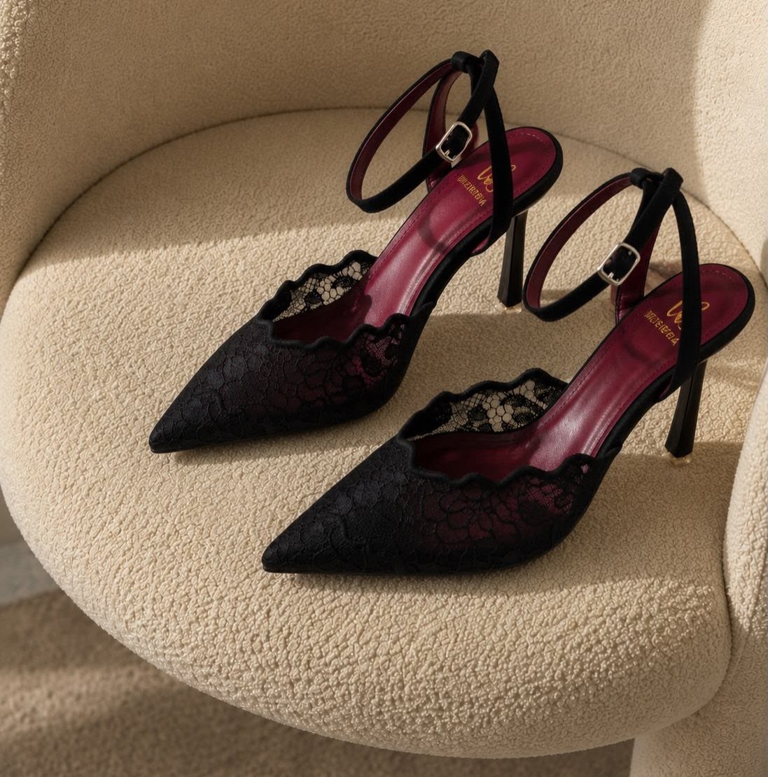 Black lace pointed-toe pumps with ankle straps on a beige textured chair