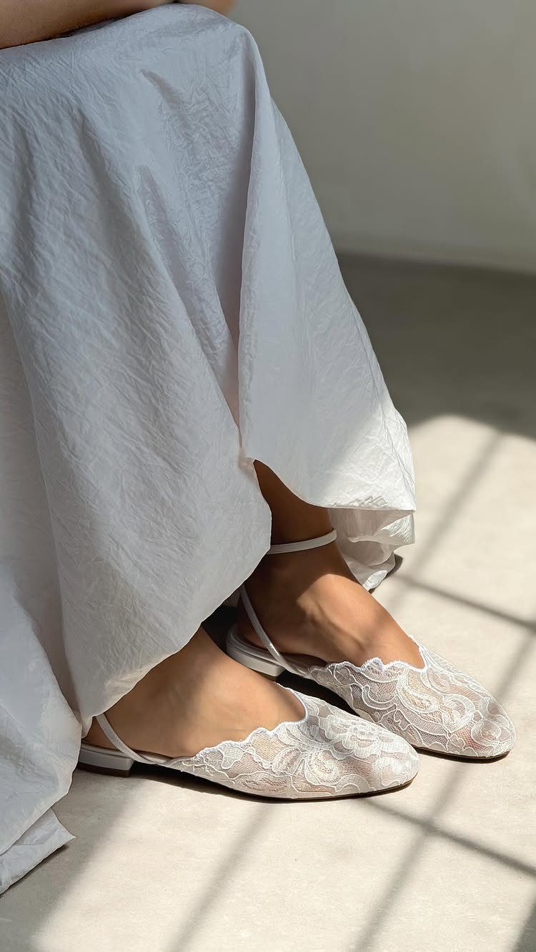 White lace flat shoes with ankle straps paired with a long white dress.