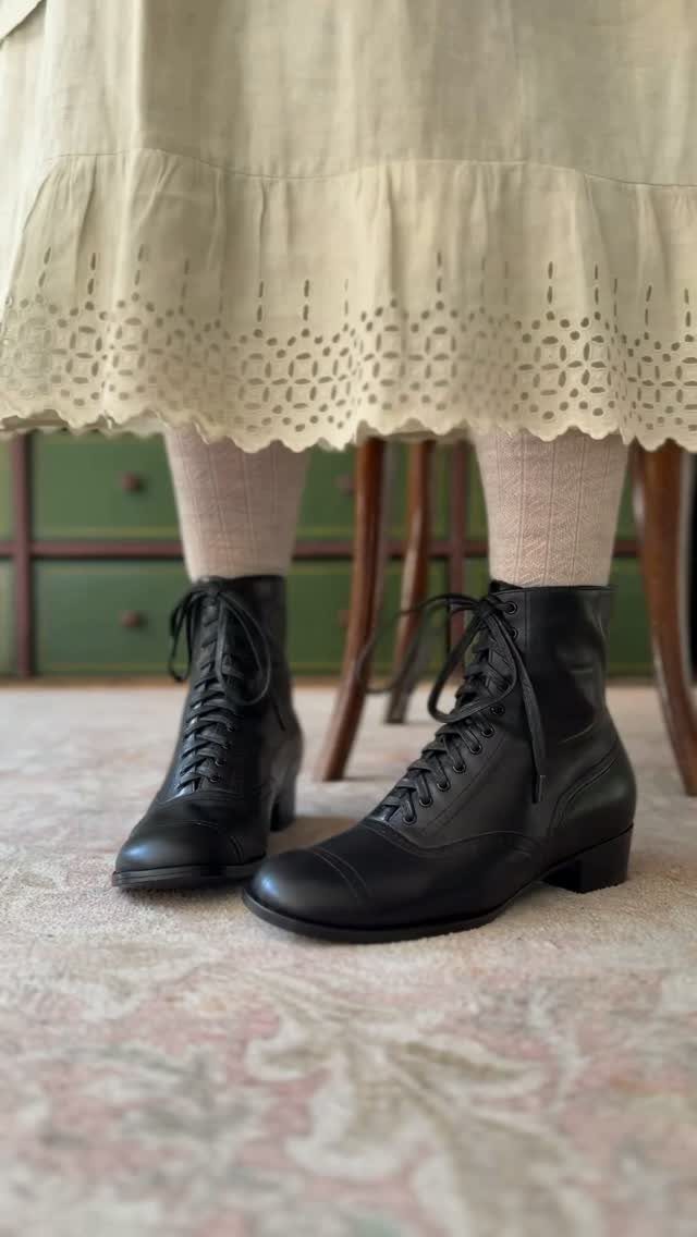 Black leather lace-up low-heeled ankle boots worn with a cream lace-hemmed dress.