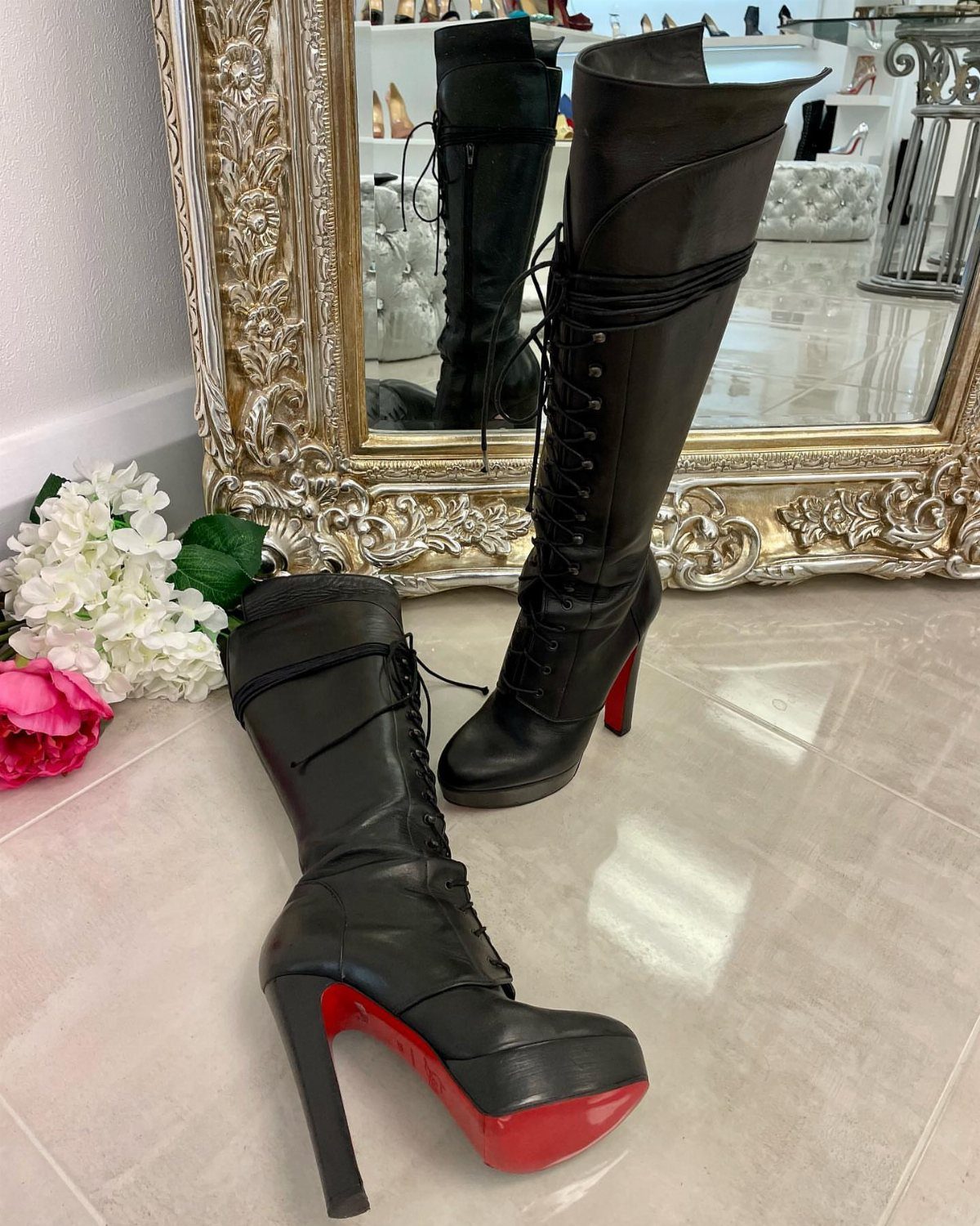 Black leather knee-high boots with slender high heels and red soles on a floor.