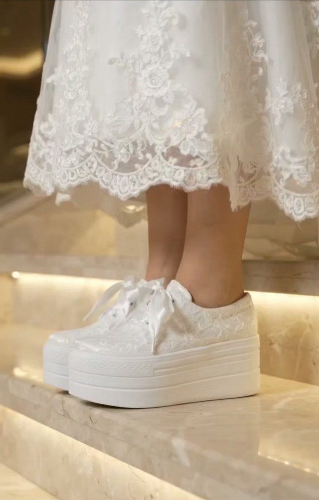 White platform lace sneakers paired with a white lace wedding dress on marble stairs.