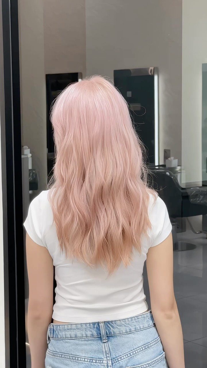 20 Summer Hair Dye Ideas, from Pastel Blue to Cool Raven 11 Woman with long wavy pastel peach hair wearing a white shirt and jeans.